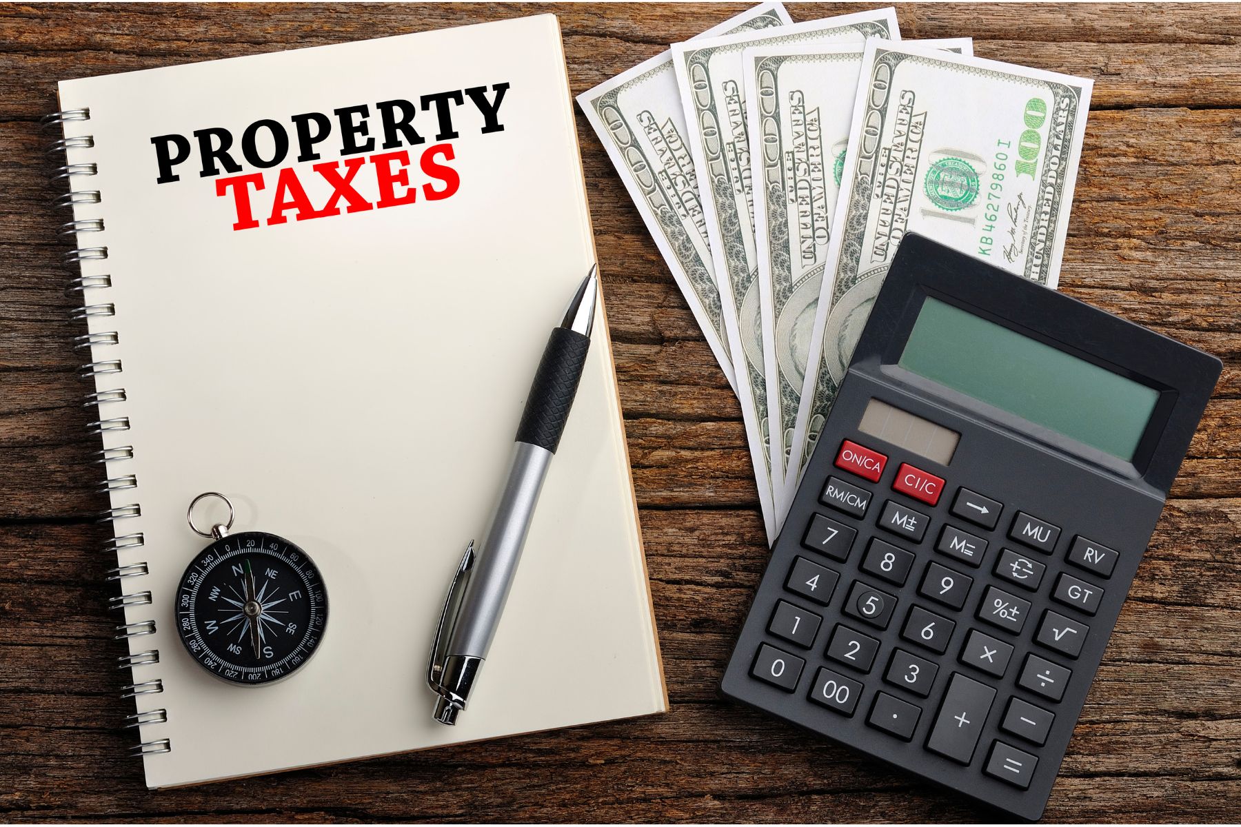 Notebook labeled Property Taxes next to cash, a calculator, and a compass, representing property tax proration in Indiana home sales.