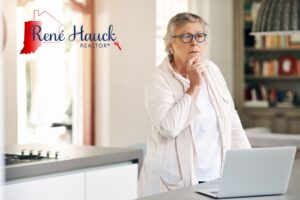 Indiana homeowner weighing the decision to sell before retirement, standing thoughtfully at kitchen counter with laptop