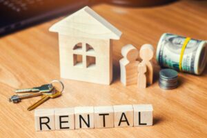 Selling a house with tenants in Indiana, a small wooden house with keys, cash, coins, and blocks spelling RENTAL