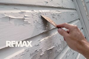 Hand scraping peeling white lead paint off the wood siding of an older Indiana home