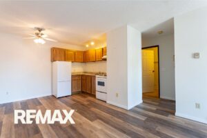Empty living room and kitchen in a vacant Indiana home with wood-look vinyl plank flooring, oak cabinets, and white appliances.